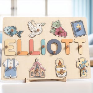 Puede incluir: Un tablero de rompecabezas de madera con el nombre "ELLIOTT" escrito en letras de colores. El tablero presenta varios s&iacute;mbolos religiosos, incluyendo una paloma, un pez, una iglesia, una cruz, una vela y uvas.