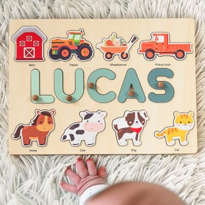 May include: A wooden personalized puzzle with the name LUCAS in large blue letters. The puzzle features farm animals and vehicles, including a barn, tractor, wheelbarrow, pickup truck, horse, cow, dog, and cat.