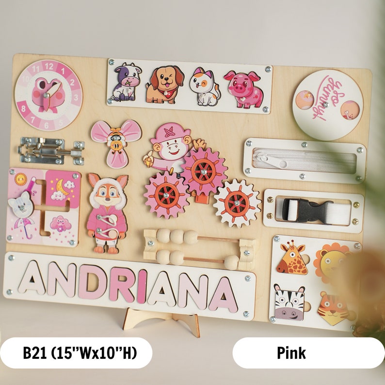 May include: Pink wooden busy board with a variety of activities for children, including a clock, a zipper, a buckle, a latch, a bead maze, gears, and animal shapes. The board is personalized with the name "ANDRIANA".