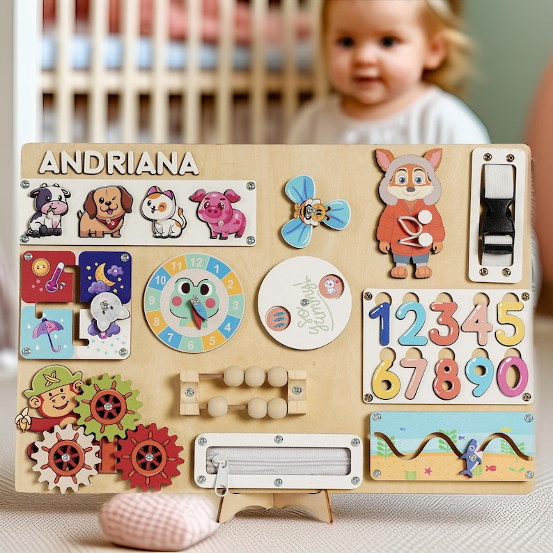 May include: Wooden activity board with various interactive elements for toddlers. Features animal figures, a clock, gears, numbers, a zipper, and the name "ANDRIANA". Includes a small abacus and a buckle. The board is designed for educational play.