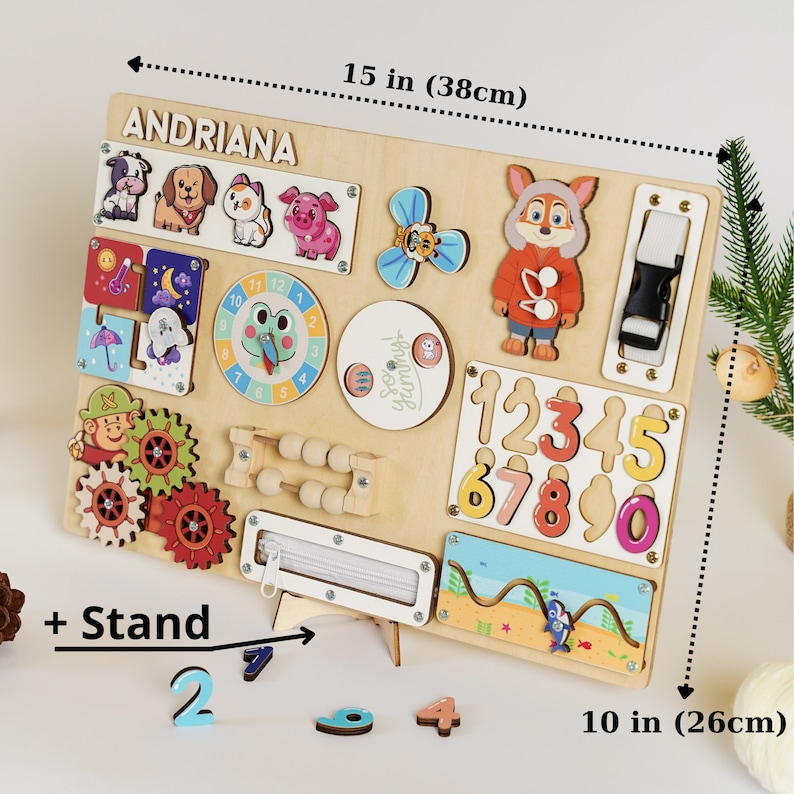 May include: A wooden activity board, 15 inches by 10 inches, featuring various interactive elements. Includes animal figures, a clock, gears, a zipper, numbers, and a fox character. The board has the name "ANDRIANA" at the top.