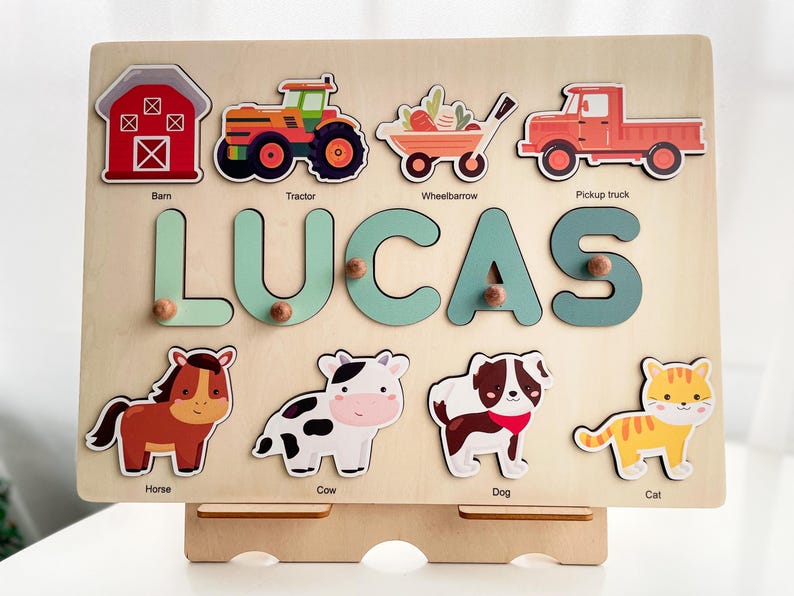 May include: A wooden educational toy with a name puzzle that says "LUCAS" and images of farm animals, vehicles, and a barn. The toy is on a stand.