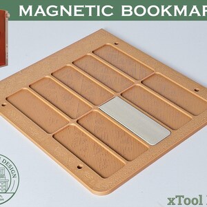 Pode incluir: Um marcador magnético castanho claro com um design retangular. O marcador tem várias ranhuras retangulares e uma placa de metal prateado. O texto "MAGNETIC BOOKMARK" está no topo.
