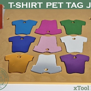 Könnte beinhalten: Eine goldfarbene T-Shirt-Haustieranhänger-Jig mit neun T-Shirt-förmigen Aussparungen in verschiedenen Farben. Der Text "T-SHIRT PET TAG JIG" steht oben. Eine orangefarbene Maschine befindet sich in der oberen linken Ecke. Der Text "xTool F1/F2" steht unten.