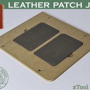 Puede incluir: Una plantilla de parche de cuero beige con dos parches de cuero gris. La plantilla tiene forma cuadrada con esquinas redondeadas y agujeros. El texto "LEATHER PATCH JIG" está en la parte superior.