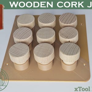 May include: A wooden cork jig for xTool F1/F2 laser machines featuring a tan rectangular base with a textured surface and nine cylindrical wooden holders arranged in a three-by-three grid. The base includes four corner screw holes for mounting.