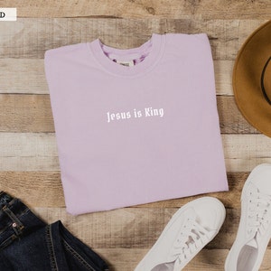 May include: A lavender sweatshirt with the text "Jesus is King" in white lettering.