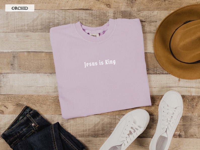 May include: A lavender sweatshirt with the text "Jesus is King" in white lettering.