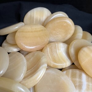 May include: A pile of smooth, oval-shaped, light yellow stones. The stones have a subtle, striated pattern.
