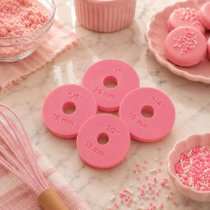 May include: Four circular pink fondant cutters with center holes, each embossed with measurements: 1/2 inch (13 mm), 5/8 inch (16 mm), 3/4 inch (19 mm), and 1 inch (25 mm). These tools are designed for precise shaping of dough or icing in baking.