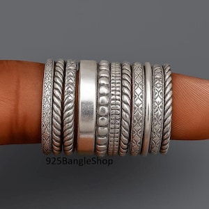 May include: A collection of silver rings with various textures and patterns, including braided, beaded, and geometric designs. The rings are stacked on a finger, showcasing the different styles. The shop name "925BangleShop" is visible.