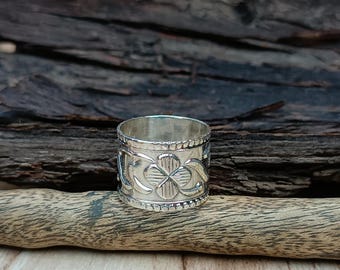 May include: A silver ring with a clover design. The ring is wide and has a textured surface.