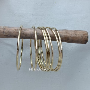 Peut inclure: Un ensemble de huit bracelets joncs dorés empilés sur une surface en bois. Les bracelets ont tous la même largeur et une finition lisse et polie.