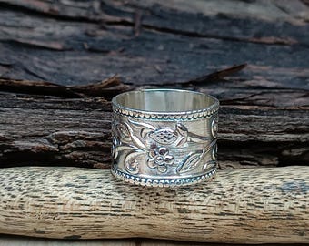 May include: A silver ring with a floral design. The ring is wide and has a textured surface.