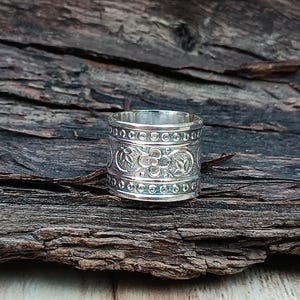 K&ouml;nnte beinhalten: Ein silberner Ring mit einem floralen Design. Der Ring ist breit und hat eine strukturierte Oberfl&auml;che.