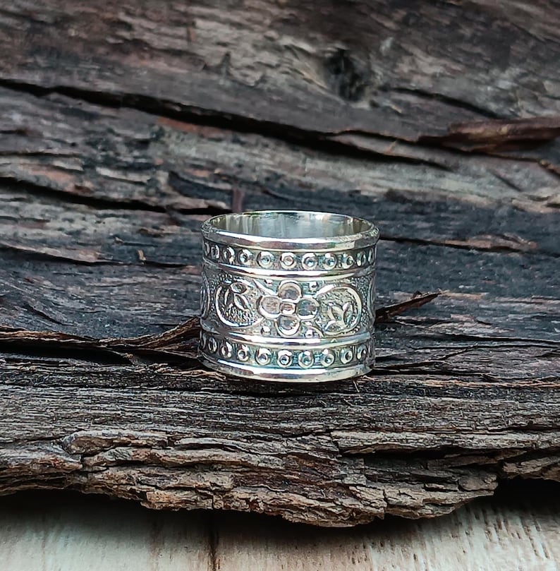 K&ouml;nnte beinhalten: Ein silberner Ring mit einem floralen Design. Der Ring ist breit und hat eine strukturierte Oberfl&auml;che.