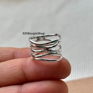 May include: A silver ring with a distinctive, layered design. The ring has multiple bands that intertwine, creating an open, woven appearance. The text "925BangleShop" is visible on the image.