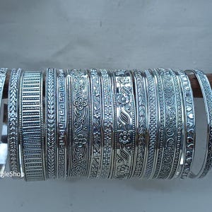 Puede incluir: Un conjunto de pulseras de plata con diseños intrincados. Las pulseras están apiladas una encima de la otra y tienen una variedad de patrones, incluyendo diseños florales, geométricos y abstractos.