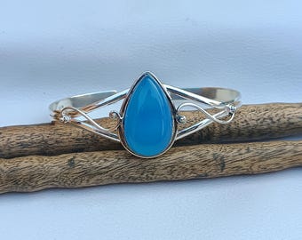 May include: A silver bracelet with a teardrop-shaped blue gemstone. The bracelet has a delicate, ornate design.
