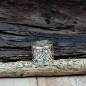 K&ouml;nnte beinhalten: Ein silberner Ring mit einem komplizierten Blumenmuster. Der Ring ist breit und hat eine strukturierte Oberfl&auml;che.