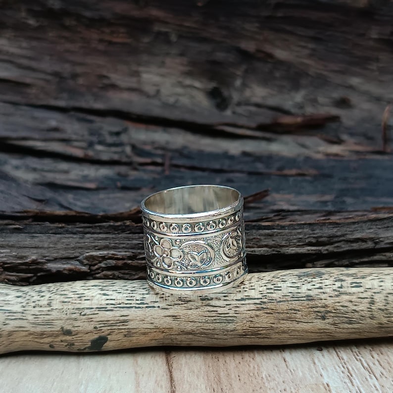 K&ouml;nnte beinhalten: Ein silberner Ring mit einem komplizierten Blumenmuster. Der Ring ist breit und hat eine strukturierte Oberfl&auml;che.