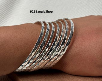 Pode incluir: Um conjunto de pulseiras de prata com textura martelada. As pulseiras estão em um pulso, com o texto "925BangleShop" visível na imagem. As pulseiras são de cor prata brilhante.