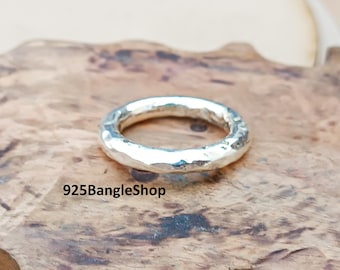 Könnte beinhalten: Ein silberner Ring mit gehammerter Textur. Der Ring ist kreisförmig und hat eine leicht unregelmäßige Oberfläche. Der Ring wird auf einer Holzoberfläche präsentiert. Der Text "925BangleShop" ist sichtbar.