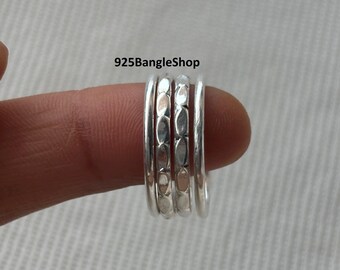 May include: A stackable silver ring set. The rings are held by a finger. The rings have a polished finish with a textured design on the center ring. The text "925BangleShop" is visible.