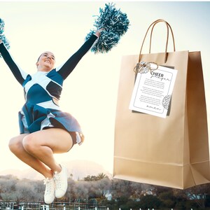 May include: A brown paper gift bag with a white card attached to it. The card has the text "Cheer Prayer" and a floral design. A cheerleader is jumping in the air in the background.