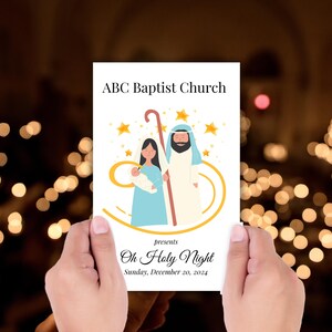 Puede incluir: Una tarjeta blanca con el texto "ABC Baptist Church" y "Oh Holy Night", con una ilustración de María, José y el niño Jesús. La tarjeta se sostiene frente a un fondo borroso de luces.