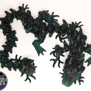May include: A black and green segmented dragon sculpture with a textured surface. The dragon is curled into a circle with its head facing forward.