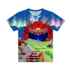 May include: A blue t-shirt featuring a pixelated image of a red demon, a car, and a monster on a road. The text "HI" is visible in the bottom left corner.