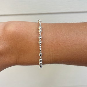 May include: A silver beaded bracelet with a simple design. The bracelet is made of small, round beads that are evenly spaced.