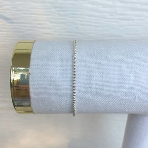 May include: A silver beaded bracelet on a white fabric display stand.
