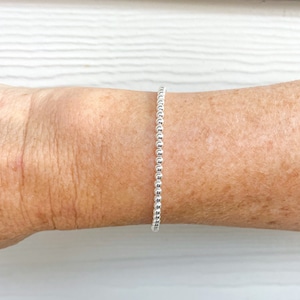 May include: A silver beaded bracelet on a person's wrist.