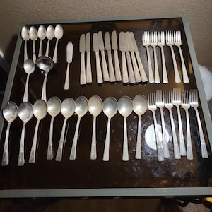 以下が含まれることがあります： ガラスの表面に並べられたフォーク、ナイフ、スプーンを含む銀食器のセット。銀食器は銀製で、磨かれた仕上げになっています。