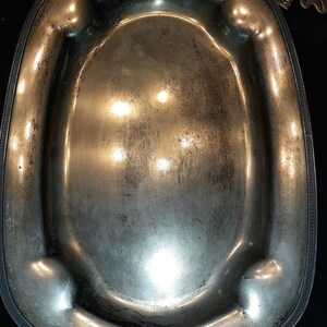 May include: A silver serving platter with a decorative border and a slightly oval shape. The platter has a worn, aged look.