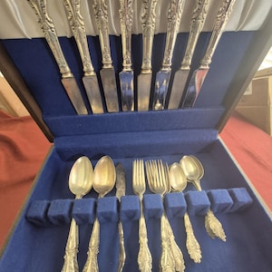 May include: A set of silver flatware in a wooden box with blue velvet lining. The set includes knives, forks, and spoons.