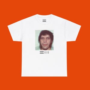 May include: White t-shirt with a mugshot of a man with dark curly hair. The image is centered on the shirt, with a small text and barcode at the bottom. The shirt is set against an orange background.