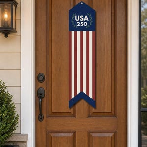 May include: A patriotic wooden door banner with a blue top section featuring the text "USA 250" and a laurel wreath design. The banner has red and white stripes, and a blue bottom section.