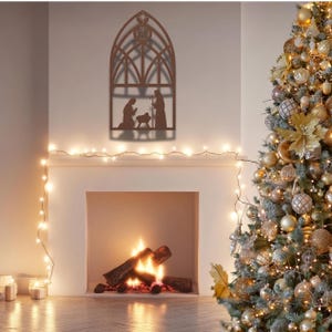 May include: A brown metal nativity scene wall hanging with an arched window design. The scene depicts Mary, Joseph, and baby Jesus. A Christmas tree with gold and silver ornaments is in the background. A fireplace with a fire is in the foreground.