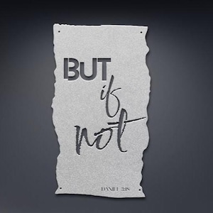 May include: A silver metal wall art piece with the words "BUT if not" cut out. The text is in a mix of block and script fonts. The bottom of the art piece has the text "DANIEL 3:18". The edges are uneven, giving it a torn paper appearance.