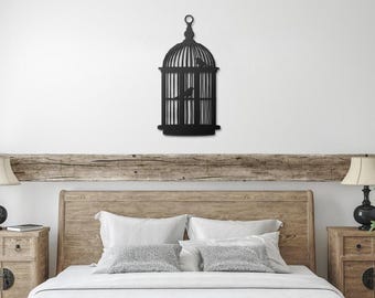 May include: Black metal birdcage wall art with a bird silhouette inside. The decorative piece is mounted on a white wall above a bed. The birdcage has a rounded top and vertical bars.