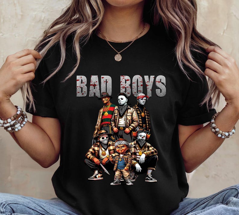 Woman wearing a black Halloween t-shirt featuring the Bad Boys of Horror PNG design with Freddy Krueger, Michael Myers, Pinhead, Jason Voorhees, Pennywise, and Chucky. The characters are dressed in brown plaid streetwear with bandanas, sneakers, and gold chains, standing under bold gray blood-splattered text that reads ‘Bad Boys.’ Horror PNG artwork displayed on apparel.