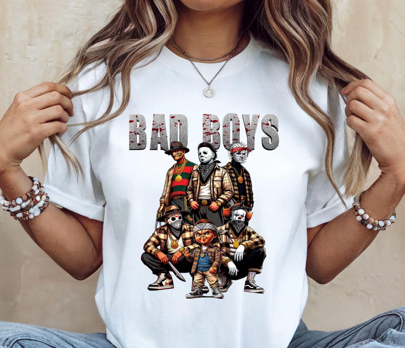 Woman wearing a white Halloween t-shirt featuring the Bad Boys of Horror PNG design with Freddy Krueger, Michael Myers, Pinhead, Jason Voorhees, Pennywise, and Chucky. The characters are dressed in brown plaid streetwear with bandanas, sneakers, and gold chains, standing under bold gray blood-splattered text that reads ‘Bad Boys.’ Horror PNG artwork displayed on apparel.