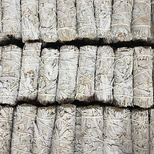 Könnte beinhalten: Nahaufnahme von mehreren Bündeln weißen Salbei-Reinigungsstäbchen. Die Stäbchen sind mit Schnur zusammengebunden und in Reihen angeordnet.