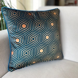 Puede incluir: Una almohada de terciopelo azul turquesa con un patr&oacute;n geom&eacute;trico dorado de hex&aacute;gonos. La almohada tiene un ribete azul turquesa.