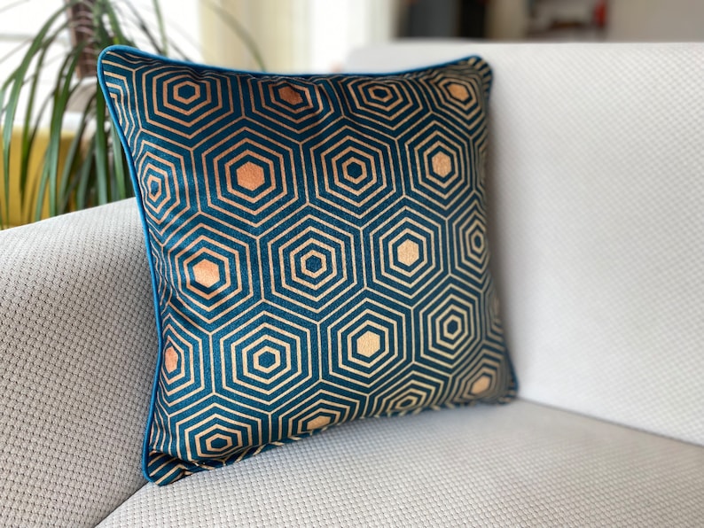 Puede incluir: Una almohada de terciopelo azul turquesa con un patr&oacute;n geom&eacute;trico dorado de hex&aacute;gonos. La almohada tiene un ribete azul turquesa.