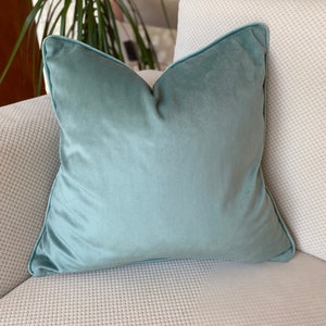 Könnte beinhalten: Ein weiches, hellblaues Kissen mit dezentem Glanz. Das Kissen liegt auf einem weißen Sofa mit strukturiertem Stoff.