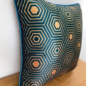 Puede incluir: Una almohada de terciopelo azul turquesa con un patr&oacute;n geom&eacute;trico dorado de hex&aacute;gonos. La almohada tiene un ribete azul turquesa.